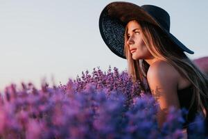 Woman lavender field. Happy carefree woman in black dress and hat with large brim smelling a blooming lavender on sunset. Perfect for inspirational and warm concepts in travel and wanderlust. Close up photo