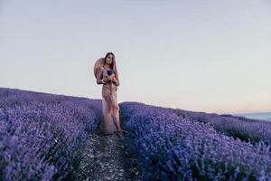 Woman lavender field. Happy carefree woman in beige dress and hat with large brim smelling a blooming lavender on sunset. Perfect for inspirational and warm concepts in travel and wanderlust. Close up photo