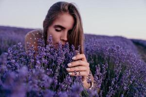 mujer lavanda campo. contento despreocupado mujer en beige vestir y sombrero con grande borde oliendo un floreciente lavanda en puesta de sol. Perfecto para inspirador y calentar conceptos en viaje y pasión de viajar. cerca arriba foto