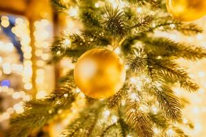 un Navidad árbol con oro adornos y luces. el árbol es decorado con oro pelotas y es iluminado arriba con luces. el árbol es metido en un habitación con un ventana foto