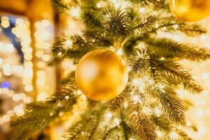 A Christmas tree with gold ornaments and lights. The tree is decorated with gold balls and is lit up with lights. The tree is placed in a room with a window photo