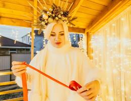 A woman in a white dress is holding a gold box with a red ribbon. She is wearing a crown on her head. The woman appears to be opening the gift box. photo