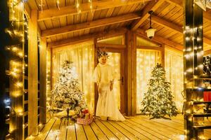 Happy smiling woman in a white dress holding a gift box in front of a Christmas tree. photo