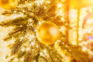 A Christmas tree with gold ornaments and lights. The tree is decorated with gold balls and is lit up with lights. The tree is placed in a room with a window photo