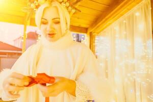 un mujer en un blanco vestir es participación un oro caja con un rojo cinta. ella es vistiendo un corona en su cabeza. el mujer aparece a ser apertura el regalo caja. foto