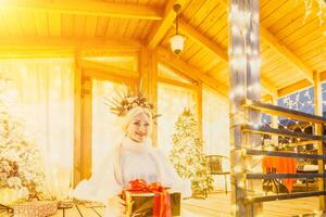 Happy smiling woman in a white dress holding a gift box in front of a Christmas tree. photo