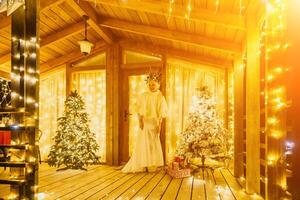 Happy smiling woman in a white dress holding a gift box in front of a Christmas tree. photo