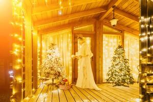 Happy smiling woman in a white dress holding a gift box in front of a Christmas tree. photo