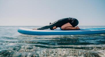 Woman sup yoga. Happy sporty woman practising yoga pilates on paddle sup surfboard. Female stretching doing workout on sea water. Modern individual female hipster outdoor summer sport activity. photo