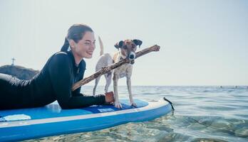 Sea woman sup. Silhouette of happy positive young woman with her dog, surfing on SUP board through calm water surface. Idyllic sunset. Active lifestyle at sea or river. Summer vacation with pets. photo