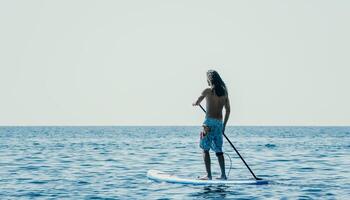 Man Sup Sea. Strong athletic man learns to paddle sup standing on board in open sea ocean on sunny day. Summer holiday vacation and travel concept. Aerial view. Slow motion photo