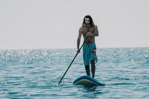 Man Sup Sea. Strong athletic man learns to paddle sup standing on board in open sea ocean on sunny day. Summer holiday vacation and travel concept. Aerial view. Slow motion photo