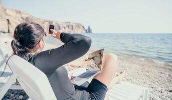 woman laptop sea. Working remotely on seashore. Happy successful lady, freelancer working on sea beach, relieves stress from work to restore life balance. Freelance, remote work on vacation photo