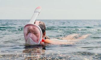 Young happy woman in white bikini and wearing pink mask gets ready for sea snorkeling. Positive smiling woman relaxing and enjoying water activities with family summer travel holidays vacation on sea. photo