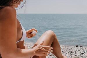 mujer protector solar mar. contento dama aplica bloqueador solar crema en bronceado piel antes de broncearse. hembra en mar vacaciones fiesta complejo. mujer utilizar Cuidado Solar loción en playa, aplicando protector solar loción en cuerpo foto