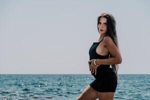 Woman summer travel sea. Happy tourist in hat enjoy taking picture outdoors for memories. Woman traveler posing on the beach at sea surrounded by volcanic mountains, sharing travel adventure journey photo