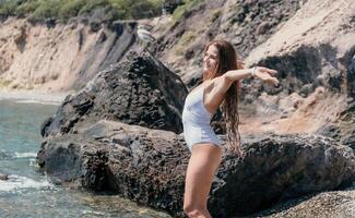 Woman travel sea. Happy tourist in white bikini enjoy taking picture outdoors for memories. Woman traveler posing on the beach at sea surrounded by volcanic mountains, sharing travel adventure journey photo