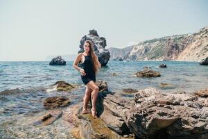 Woman summer travel sea. Happy tourist in hat enjoy taking picture outdoors for memories. Woman traveler posing on the beach at sea surrounded by volcanic mountains, sharing travel adventure journey photo