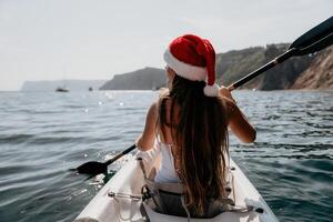 Woman in kayak back view. Happy young woman in Santa hat floating in kayak on calm sea. Summer holiday vacation and cheerful female people relaxing having fun on the boat. photo