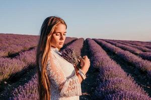 mujer lavanda campo. contento despreocupado mujer en un blanco vestir caminando en un lavanda campo y oliendo un lavanda ramo de flores en puesta de sol. ideal para calentar y inspirador conceptos en pasión de viajar y viajar. foto