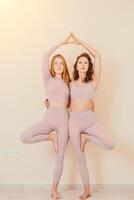 Well looking middle aged sporty woman, fitness instructor in pink sportswear doing stretching and pilates on yoga mat in the studio with mirror. Female fitness yoga. Healthy lifestyle and harmony. photo