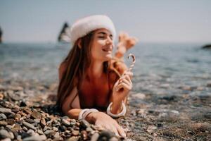 Woman travel sea. Happy tourist enjoy taking picture on the beach for memories. Woman traveler in Santa hat looks at camera on the sea bay, sharing travel adventure journey photo