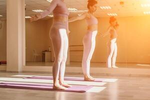 Well looking middle aged sporty woman, fitness instructor in pink sportswear doing stretching and pilates on yoga mat in the studio with mirror. Female fitness yoga. Healthy lifestyle and harmony. photo