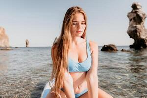 mujer mar sorber. cerca arriba retrato de contento joven caucásico mujer con largo pelo mirando a cámara y sonriente. linda mujer retrato en un azul bikini posando en cenar tablero en el mar foto