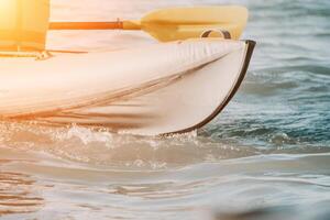 Happy couple kayaks in an inflatable kayak on the sea at sunset. Couple kanoeing in the sea near the island with mountains. People kayaking in life jackets sail. Back view photo