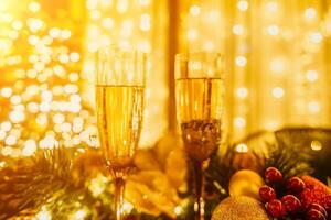 Two champagne glasses filled with champagne are placed on a table near to Christmas tree. The glasses are surrounded by lights, creating a festive atmosphere. photo