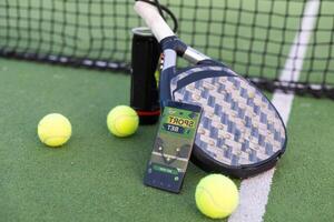 A tennis ball, a racket and a mobile phone with a put screen lie on a blue background. The concept of advertising a tennis club or ordering services. Horizontal photo