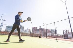 un niña en ropa de deporte es formación en un paleta tenis corte. el niña es golpear el pelota en contra el vaso a hacer un rebote. concepto de mujer jugando paleta. foto