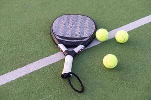 Yellow balls on grass turf near padel tennis racket behind net in green court outdoors with natural lighting. Paddle is a racquet game. Professional sport concept with copy space. photo