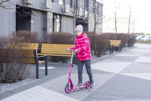 Little cute girl riding a scooter on a path in the park photo