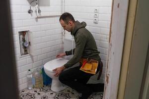 Repairman hands installing flush toilet, toilet bowl in the bathroom photo