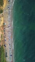 antenne visie van zanderig strand, zwemmen mensen in zee baai met transparant blauw water Bij zonsondergang in zomer. gelukkig mensen menigte ontspannende Aan strand. vakantie recreatie oceaan natuur concept. verticaal video