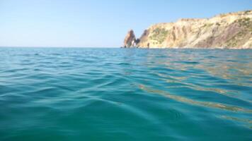 Meer Wasser Oberfläche. Kamera fliegt Über das Ruhe azurblau Meer mit vulkanisch felsig Ufer auf Hintergrund. niemand. Urlaub Erholung Konzept. abstrakt nautisch Sommer- Ozean Natur. schleppend Bewegung. schließen oben video