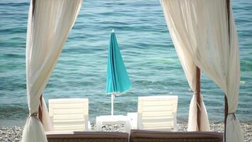 Bungalows sea. Beach Lounge bed with white silky curtains. Empty Lounge bed with canopy at seaside. Beach Chairs and Sunshades. Summer Vacation resort concept. Nobody. Slow motion video