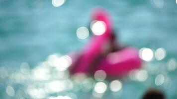 abstract onscherp zomer vakantie vrouw drijft Aan opblaasbaar roze flamingo, water speelgoed- zwemmen ring. positief gelukkig vrouw ontspannende en genieten van familie zomer reizen vakantie vakantie Aan zee. langzaam beweging video