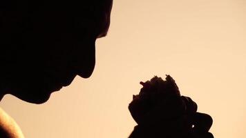 Silhouette of a man enjoying a hamburger. Side view portrait of a person savoring a delicious, satisfying burger with great appetite. Fast food indulgence. video