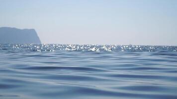 Sea water surface. Camera flies over the calm azure sea with volcanic rocky shores on background. Nobody. Holiday recreation concept. Abstract nautical summer ocean nature. Slow motion. Close up video