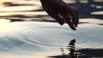 Woman hand sea. Close-up Happy Woman gently caresses water surface at sunset in a warm, golden evening by the sea or lake. Slow-motion Concept of happiness, boat life and holidays in exotic places video