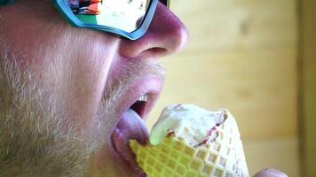 Man eating ice cream. Close-up portrait of young hipster man in sunglases eating ice cream in summer hot weather on the beach, have fun and good mood. video