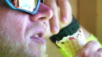 Mann Essen Eis Creme. Nahansicht Porträt von jung Hipster Mann im Sonnenbrillen Essen Eis Sahne im Sommer- heiß Wetter auf das Strand, haben Spaß und gut Stimmung. video