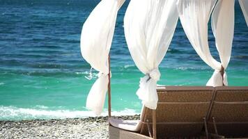 bangalôs mar. de praia salão cama com branco sedoso cortinas. salão cama com marquise às à beira-mar. de praia cadeiras e guarda-sóis. verão período de férias recorrer conceito. video