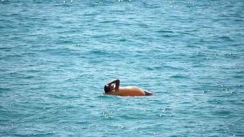 Summer Vacation man floats on an inflatable donut mattress, a water toy swim ring. Positive happy man relaxing and enjoying family summer travel holidays vacation on the sea. Slow motion video