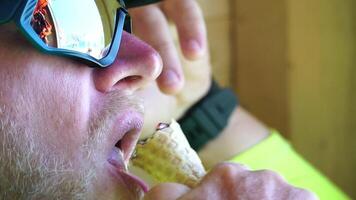 hombre comiendo hielo crema. de cerca retrato de joven hipster hombre en gafas de sol comiendo hielo crema en verano caliente clima en el playa, tener divertido y bueno humor. video