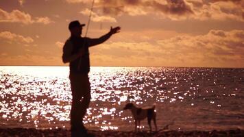 homem em pé em cais, segurando uma pescaria Cajado e preparando para fundida isto para dentro mar oceano às caloroso pôr do sol. homem passatempo pescaria em mar aperta uma pescaria linha bobina do peixe verão. calma superfície mar. lento movimento. video