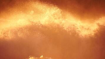 Storm Wave Sunset. Large wave crashing into shore, creating foam and spray at golden burning sunset. Seascape with storm breaking waves. Weather and climate change video