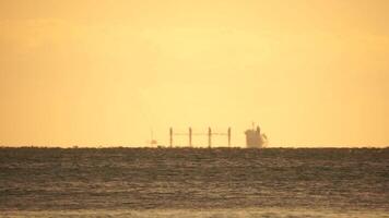 Mirage of cargo ship in the sea beyond the horizon. Ship sailing in the sea. Small waves on the golden surface of warm water with bokeh lights from the sun. Sea, nature and outdoor travel. video